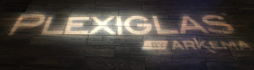 "Plexiglas by Arkema" written in light, on a dark wood floor.